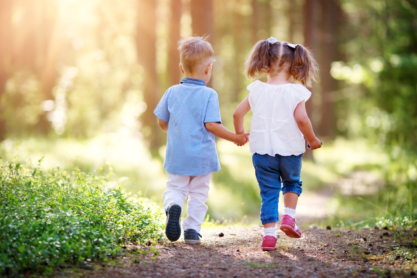 a toddler boy and girl walking a path together in the woods